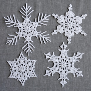 Peut inclure: Quatre flocons de neige en crochet blanc sur un fond de lin gris. Les flocons de neige sont tous de formes et de tailles diff&eacute;rentes.