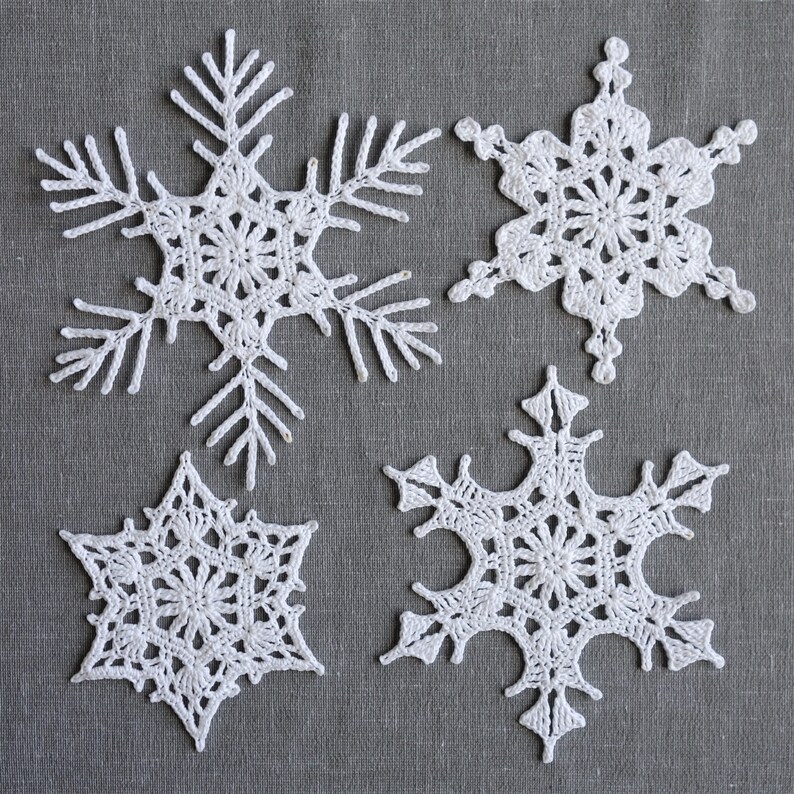Peut inclure: Quatre flocons de neige en crochet blanc sur un fond de lin gris. Les flocons de neige sont tous de formes et de tailles diff&eacute;rentes.