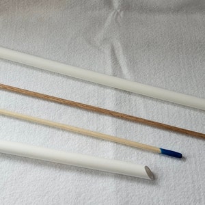 May include: Three white dowel rods with blue tips, two are shorter and one is longer. The shorter rods are lying on a white surface, while the longer rod is leaning against the surface.
