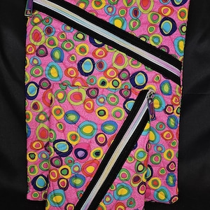 May include: A set of three pink fabric pouches with a colorful, abstract pattern of overlapping circles in shades of blue, green, yellow, and orange. Each pouch has a black zipper with a silver pull. The number "197" is printed in the bottom right corner.