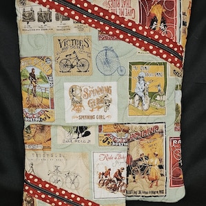 May include: A quilted pouch with a bicycle theme. The light green fabric is decorated with vintage bicycle advertisements and illustrations. A red zipper with white polka dots and a black zipper pull diagonally bisects the pouch.