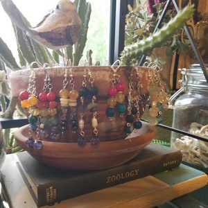 May include: A collection of colourful beaded earrings with silver hooks. The earrings are displayed in a terracotta pot on a shelf with books.
