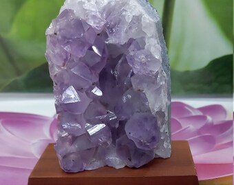 Könnte beinhalten: Ein großer Amethyst-Kristall-Cluster mit einem violetten und weißen Farbschema. Der Kristall wird auf einem Holzsockel präsentiert.