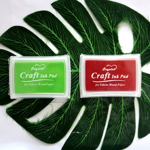 May include: Two craft ink pads, one green and one red, with the text "Crystal Craft Ink Pad for Fabric. Wood. Paper" on each.