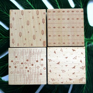 May include: Four wooden blocks featuring different patterns. The designs include trees, birds, geometric shapes, and lines. The blocks are all made of light wood and have a natural finish.