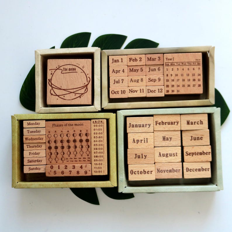 K&ouml;nnte beinhalten: Vier Holzkisten mit S&auml;tzen von Gummistempeln zum Basteln und Scrapbooking. Die Boxen enthalten Stempel f&uuml;r Wochentage, Monate des Jahres, Mondphasen, Zahlen und einen Stempel mit der Aufschrift "The meme".