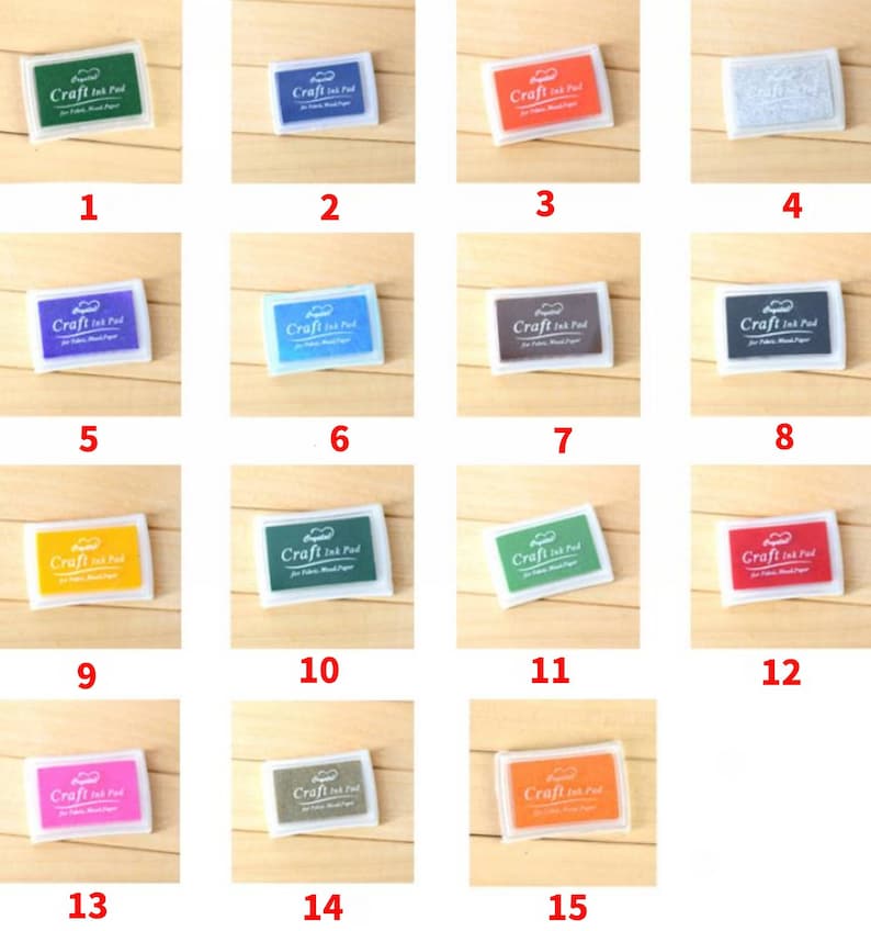 May include: Fifteen small, square, white plastic ink pads with different colored ink inside. The ink pads are labeled "Craft Ink Pad" and are arranged in a grid of five rows and three columns.