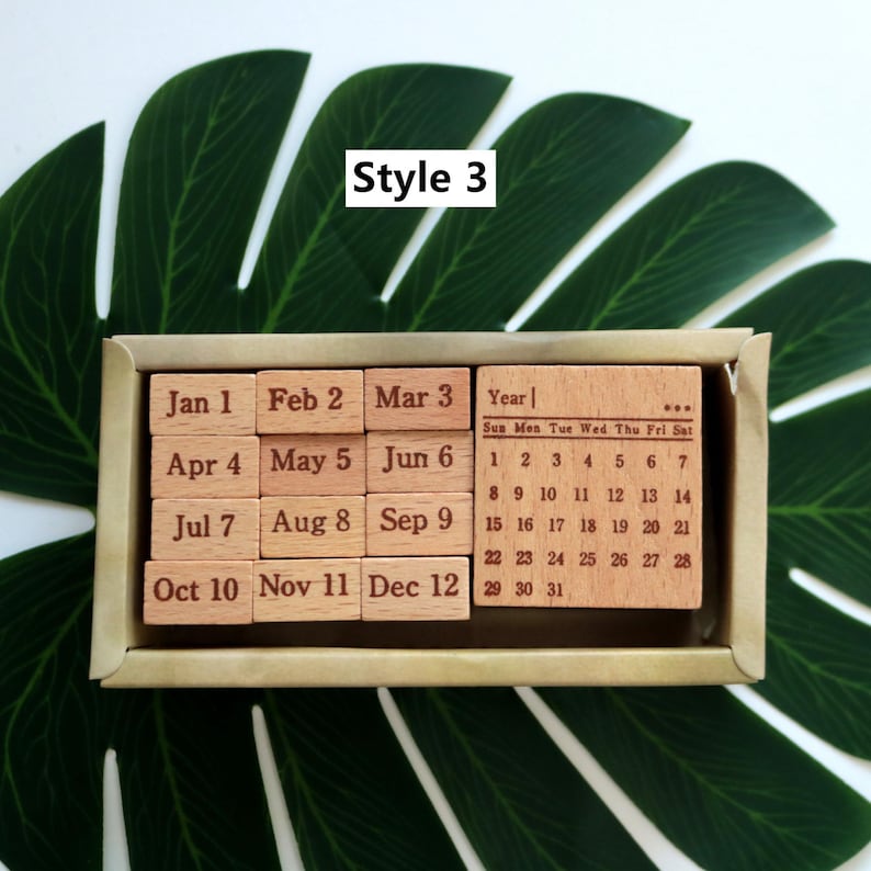 K&ouml;nnte beinhalten: Ein Satz mit 12 Holzstempeln mit den Monaten des Jahres und den Zahlen 1 bis 31. Die Stempel sind in einer Holzkiste angeordnet. Die Kiste tr&auml;gt die Aufschrift "Style 3" auf der Oberseite.