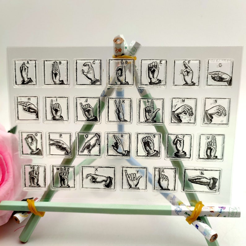May include: A clear sheet with 26 alphabet letters in American Sign Language. Each letter is in a square frame and is printed in black ink.