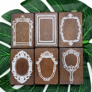Può includere: Sei timbri in legno con cornici ornate, ognuno con un design diverso. Le cornici sono bianche su sfondo marrone. I timbri sono disposti in due file da tre.