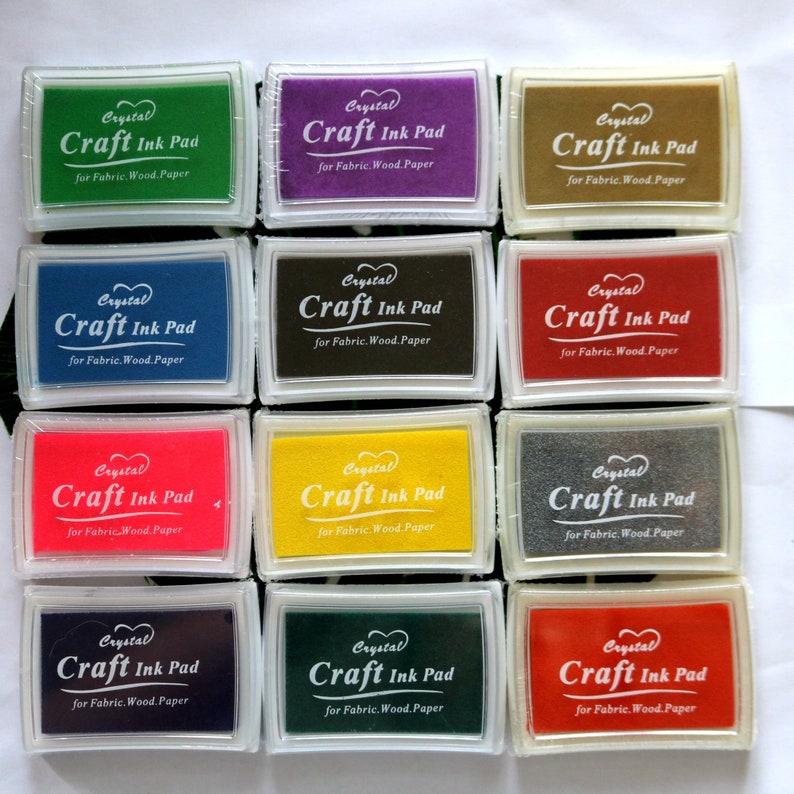 May include: Twelve craft ink pads in various colors, including red, yellow, green, blue, black, and purple. Each pad has a clear plastic case with the text "Crystal Craft Ink Pad for Fabric. Wood. Paper" printed on it.