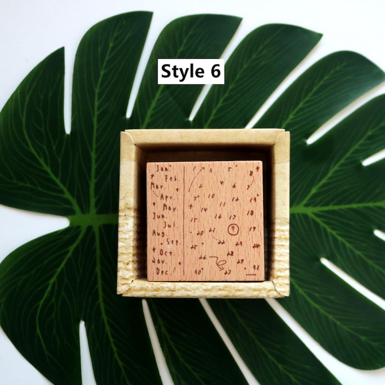 K&ouml;nnte beinhalten: Ein Stempel aus Holz mit einem Kalenderdesign. Der Stempel befindet sich in einer Holzkiste. Der Kalender hat die Monate des Jahres auf der linken Seite und die Tage des Monats auf der rechten Seite aufgelistet. Der Stempel ist mit "Style 6" gekennzeichnet.