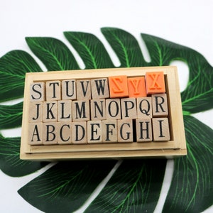 May include: A wooden box filled with alphabet letter blocks. The letters S, Y, and X are highlighted in orange.