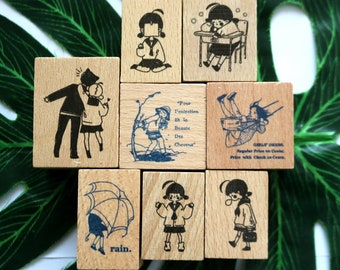 Puede incluir: Conjunto de diez sellos de madera con ilustraciones de personas y texto. Los sellos son rectangulares y de color marrón claro. Las ilustraciones son en blanco y negro e incluyen una niña con una coleta, una niña en un columpio, una niña con un paraguas, una niña con un libro, una niña con una flor, una niña con un vestido, una niña con un sombrero, una niña con un lazo, una niña con un corazón y una niña con una estrella. El texto en los sellos incluye "Pour l'entretien et la beaute des cheveux", "Girls Dress", "Rain", y "Check in Cents".
