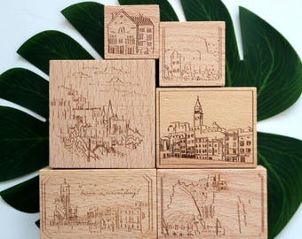 May include: Set of five wooden stamps featuring different cityscapes. Each stamp has a unique design with detailed line drawings of buildings and architecture. The stamps are made of natural wood and have a rustic, vintage aesthetic.