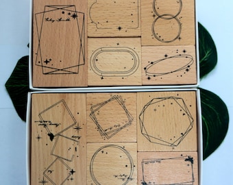 May include: Set of 10 wooden stamps with geometric designs and celestial elements. The stamps are in a white box and feature various shapes, including circles, squares, and rectangles. Each stamp has a unique design with a black outline and small stars.