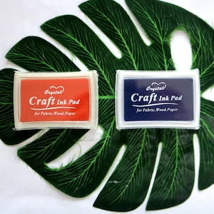 May include: Two craft ink pads, one red and one blue, with the text "Crystal Craft Ink Pad for Fabric. Wood. Paper" on each.