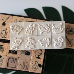 May include: A set of vintage-style rubber stamps with various designs, including a teapot, ice cream cone, gramophone, and camera. The stamps are arranged in a wooden box, perfect for crafting and scrapbooking projects.