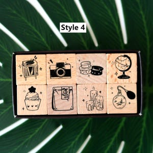May include: A set of eight wooden stamps with black ink illustrations. The stamps feature a record player, camera, stacked desserts, a globe, a cupcake, a bag with "Thank you" text, candles, and a perfume bottle. The text "Style 4" is in the top left corner.