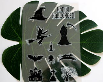 May include: A clear sheet of transparent stamps with black Halloween themed images. The images include a witch on a broomstick, a ghost, a bat, a spider, a haunted house, a graveyard cross, a tree, a candle, a witch's hat, and the text "Happy Halloween".