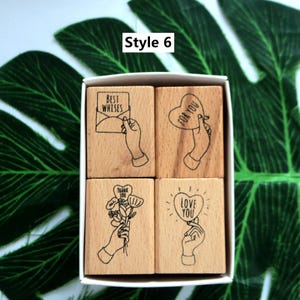 May include: Set of four wooden stamps with illustrations of hands holding various objects. The stamps feature the text "Best Wishes", "For You", "Thank You", and "Love You".