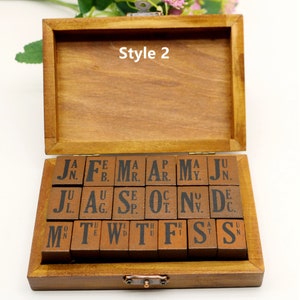 Puede incluir: Una caja de madera con tapa abatible que contiene un juego de sellos de letras y n&uacute;meros. Los sellos est&aacute;n dispuestos en filas y son de madera con tinta negra. La caja est&aacute; etiquetada como "Style 2".