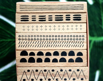 Könnte beinhalten: Ein Satz Holzstempel mit verschiedenen geometrischen Mustern. Die Stempel sind in einem Stapel angeordnet und zeigen schwarz-weiße Designs, darunter Linien, Punkte und Formen.