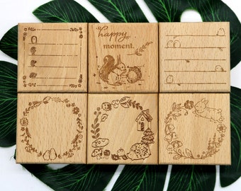 May include: Six wooden stamps with different designs. The stamps feature a squirrel, a bird, a wreath, a house, a hedgehog, and a rabbit. The stamps are all made of light brown wood and have a natural finish.