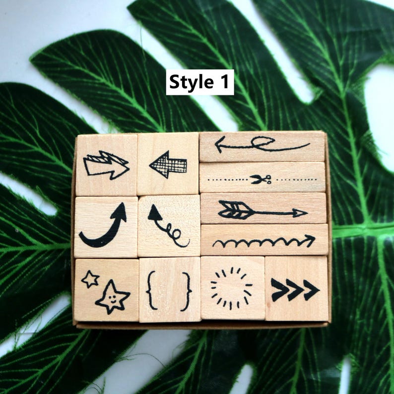 May include: A set of 12 wooden stamps featuring a variety of arrow, star, sun, and other designs. The stamps are arranged in a wooden box. The box is labelled "Style 1".