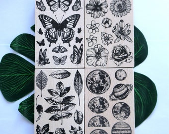 May include: Set of four wooden stamps featuring black and white illustrations of butterflies, flowers, leaves, and moons. The stamps are approximately 2 inches by 2 inches.