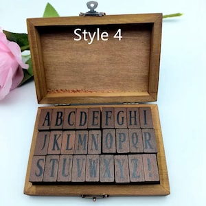 Puede incluir: Una caja de madera con tapa con bisagras, que contiene un juego de 26 sellos de letras del alfabeto y un sello de signo de exclamaci&oacute;n. La caja est&aacute; etiquetada como "Style 4".
