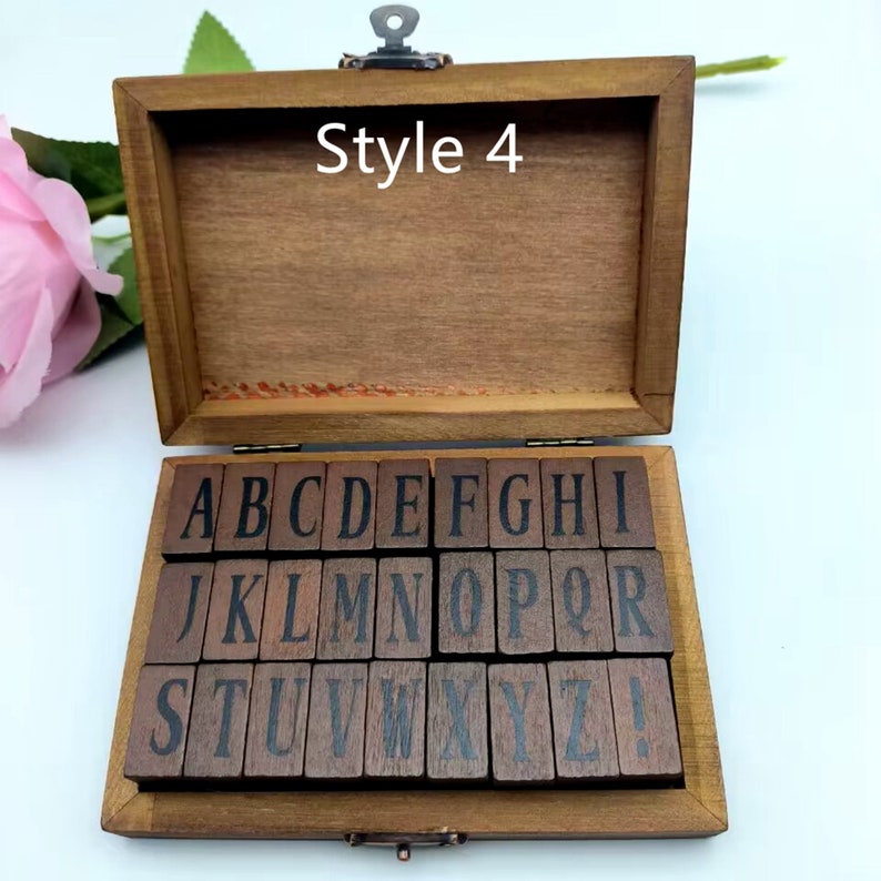 Puede incluir: Una caja de madera con tapa con bisagras, que contiene un juego de 26 sellos de letras del alfabeto y un sello de signo de exclamaci&oacute;n. La caja est&aacute; etiquetada como "Style 4".