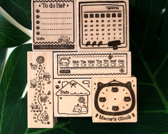 Puede incluir: Un conjunto de sellos de madera con diseños de gatos. Los sellos incluyen una lista de tareas, un calendario, un planificador semanal, una casa y un reloj. El texto incluye "Have a nice day" y "Meow's Clock".