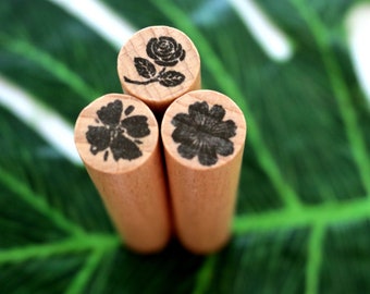 May include: Three wooden stamp blocks with black floral designs. The stamps feature a rose, a hibiscus, and a five-petal flower.