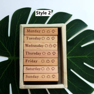 K&ouml;nnte beinhalten: Holzb&ouml;cke mit den Tagen der Woche, einem Sonnen- und Wolken-Symbol und dem Text "Style 2".