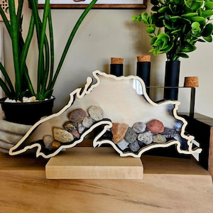 Peut inclure: Une découpe en bois du lac Supérieur avec un insert en acrylique transparent rempli de petites pierres. La découpe est sur une base en bois.