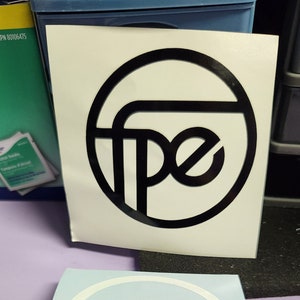May include: Two white vinyl stickers with a black circle and the letters "pe" inside. The stickers are on a purple surface.