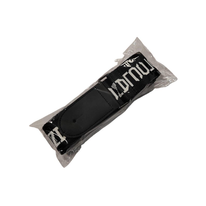 K&ouml;nnte beinhalten: Schwarzer Gitarrengurt mit wei&szlig;em Text und einem schwarzen Schulterpolster aus Leder. Der Gurt ist in klarem Kunststoff verpackt. Der wei&szlig;e Text lautet "IDRGO".