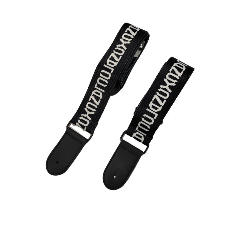 K&ouml;nnte beinhalten: Zwei schwarze Gitarrengurte mit wei&szlig;em Text "ZUXOZDRQ". Jeder Gurt hat ein schwarzes Lederendst&uuml;ck und silberfarbene Metallbeschl&auml;ge. Die Gurte sind vor einem wei&szlig;en Hintergrund abgewinkelt.
