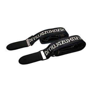 K&ouml;nnte beinhalten: Zwei schwarze Gitarrengurte mit wei&szlig;em Text "DRNUZUXOZDRNUJ". Die Gurte haben schwarze Lederenden und silberfarbene Metallbeschl&auml;ge. Auf wei&szlig;em Hintergrund.