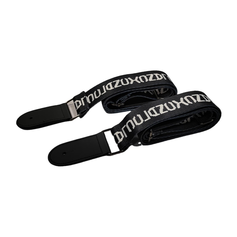 K&ouml;nnte beinhalten: Zwei schwarze Gitarrengurte mit wei&szlig;em Text "DRNUZUXOZDRNUJ". Die Gurte haben schwarze Lederenden und silberfarbene Metallbeschl&auml;ge. Auf wei&szlig;em Hintergrund.