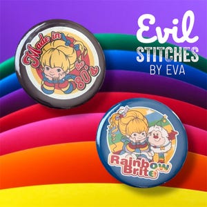 May include: Two round button badges featuring a cartoon character with blonde hair and a blue dress. The first badge has a brown background with the text "Made in the 80's". The second badge has a blue background with the text "Rainbow Brite".