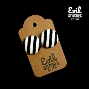 Puede incluir: Un par de pendientes de tela a rayas blancas y negras en una tarjeta marrón con el texto "Evil Stitches by Eva".