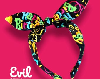 May include: Black headband with a colorful "Happy Birthday" print. The headband is tied in a bow at the top.