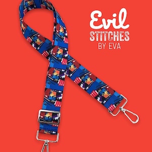May include: A blue and red patterned adjustable strap with silver hardware. The strap features a repeating pattern of a colorful illustration of a person playing a drum. The strap is labeled "Evil Stitches by Eva".