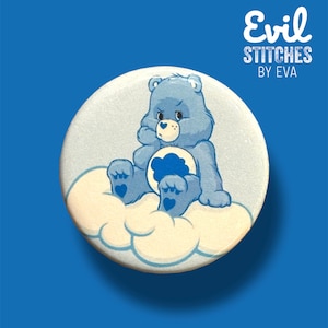 May include: A blue Care Bear with a sad expression sits on a white cloud. The bear is holding a blue cloud in its paws. The text "Evil Stitches by Eva" is written in white on a black background above the bear.