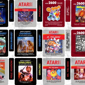 May include: A collection of Atari 2600 video game cartridge labels featuring various titles including Video Pinball, Phoenix, Q-bert, Millipede, Yars' Revenge, Space Invaders, Defender, Jr. Pac-Man, Pole Position, Pac-Man, Warlords, Ms. Pac-Man, and Swordquest.