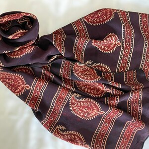 May include: A dark brown paisley patterned scarf with red and cream accents. The scarf is made of a soft, lightweight fabric and is perfect for adding a touch of style to any outfit.