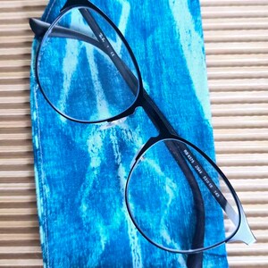 May include: Black framed glasses with clear lenses resting on a blue and white patterned fabric case. The glasses have the text "RB 8375 2944 53□18 145" printed on the arm.