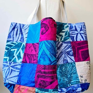 May include: A large patchwork tote bag with a variety of blue, pink, and green patterns. The bag has a white canvas strap.